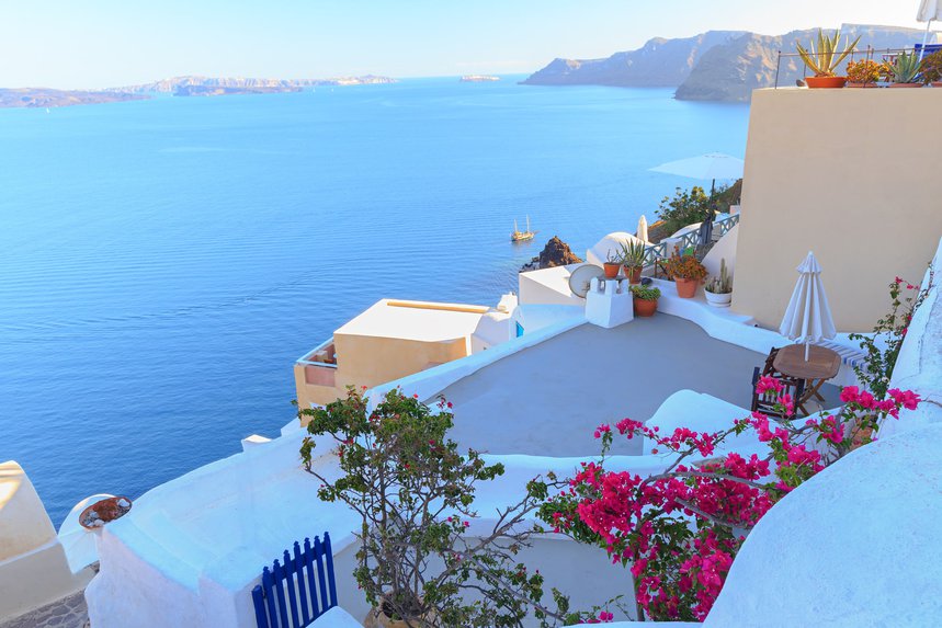 A view over the sea from a whitewashed terrace with pink flowers.
