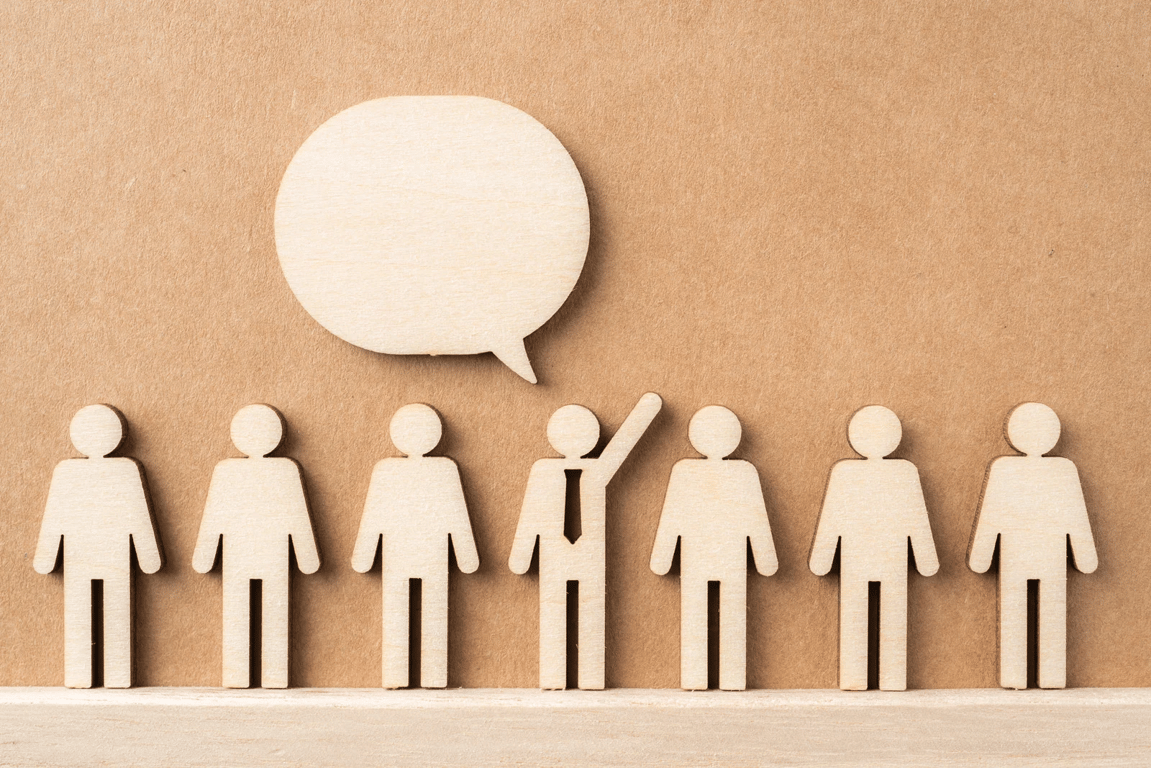 Wooden figures with one raising a hand under a speech bubble, illustrating a conversion event.